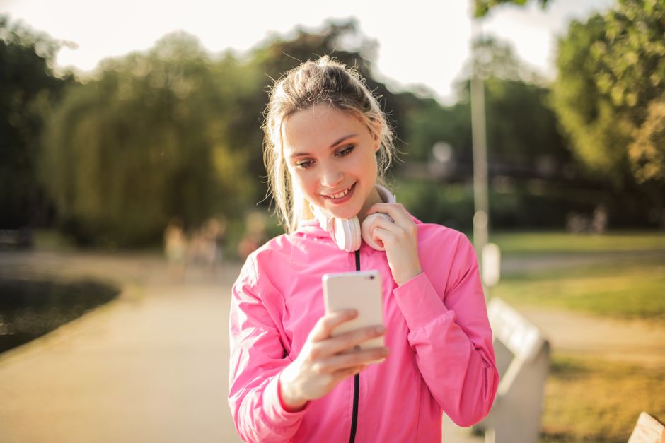 Young woman with headphones enjoying a pleasant day outside while texting on her smartphone.
