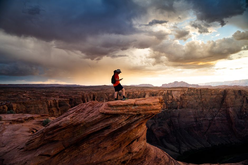 A hiker exploring a canyon in Arizona at sunrise, showcasing a dramatic sky and scenic landscape.