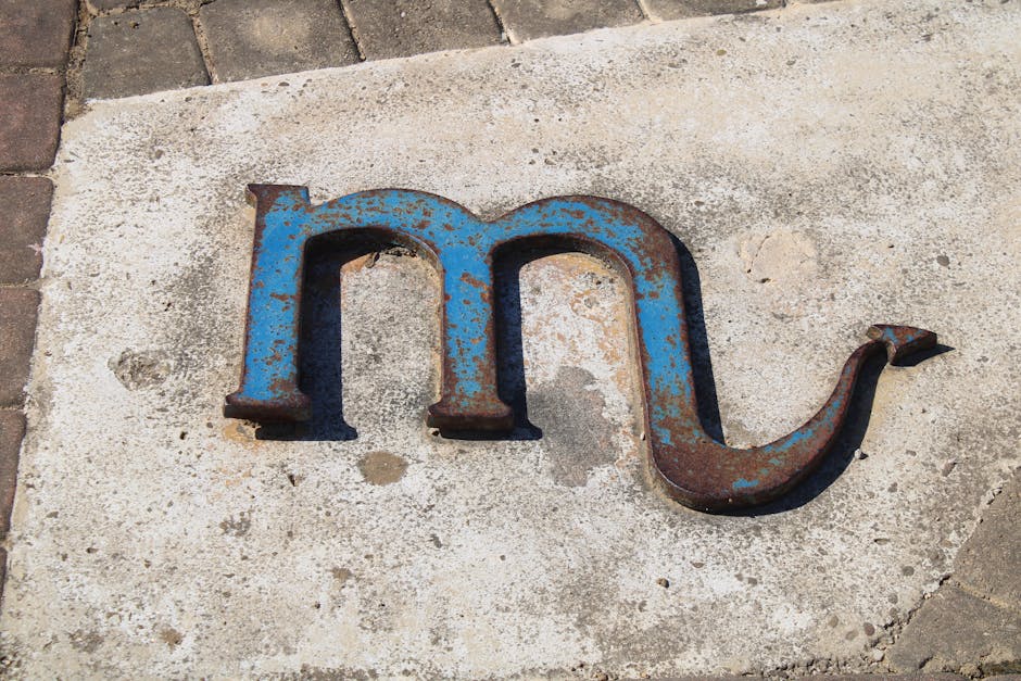 Weathered metal letter M with rust on concrete, captured in Puerto Real, España.