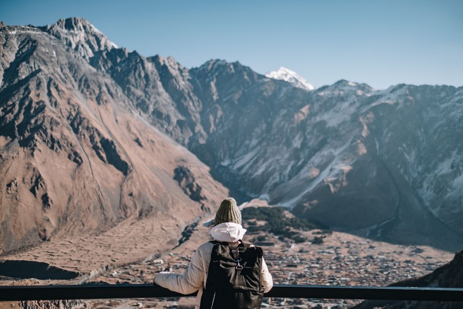 A hiker with a backpack enjoys the scenic mountain range view in Stepantsminda, Georgia.