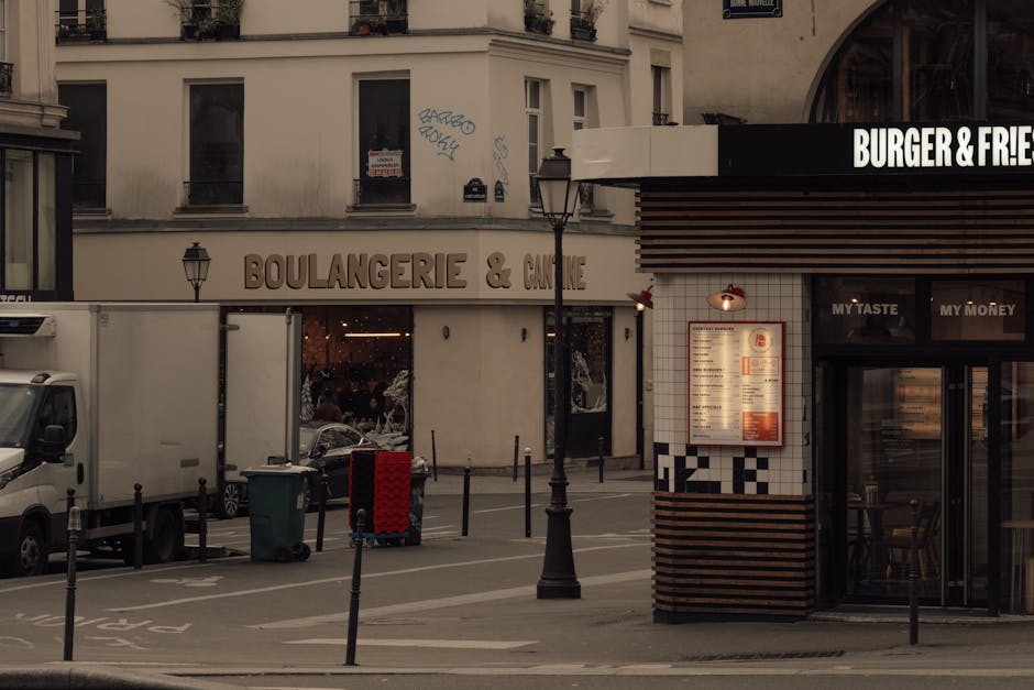 Evening view of a Paris street corner featuring a boulangerie and a burger shop, capturing city life and French architecture.
