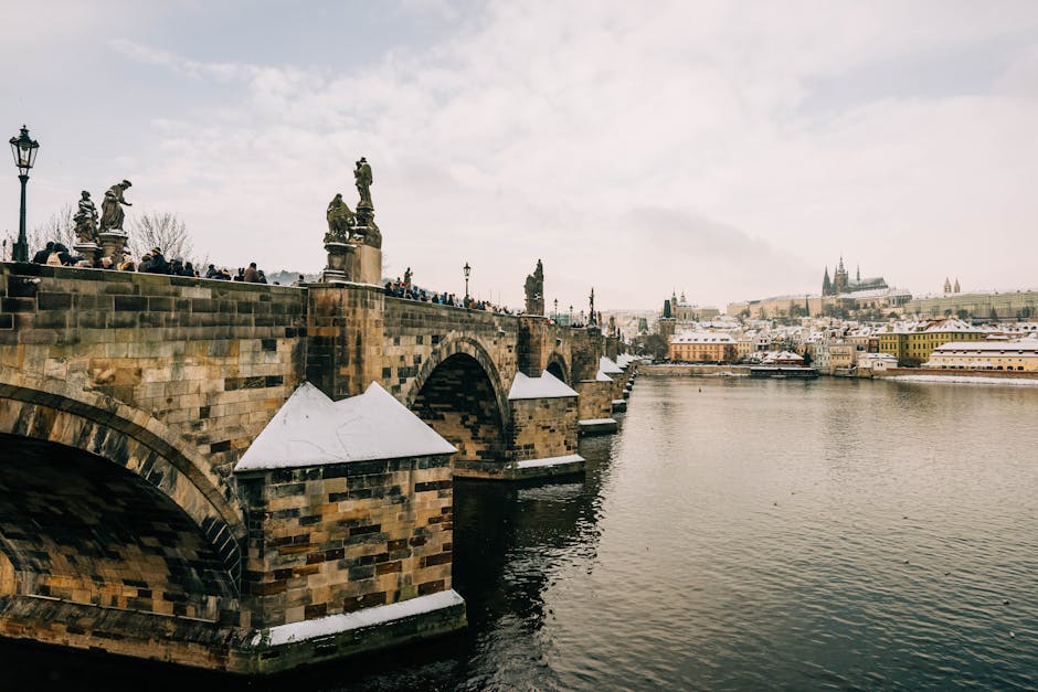 Charming winter scene of the Charles Bridge and river with snowy rooftops in Prague.