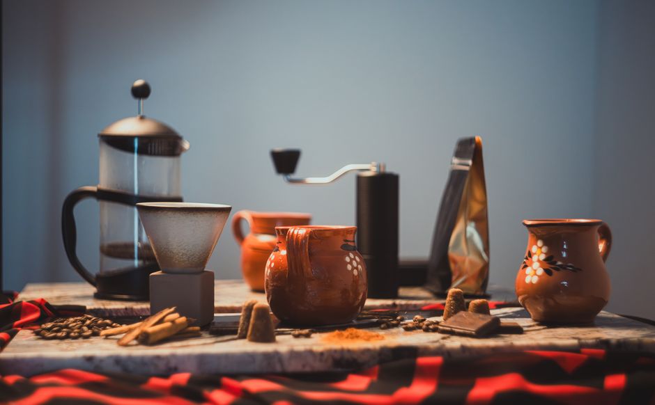 A cozy artisan coffee setup featuring traditional pottery mugs, grinder, and French press.