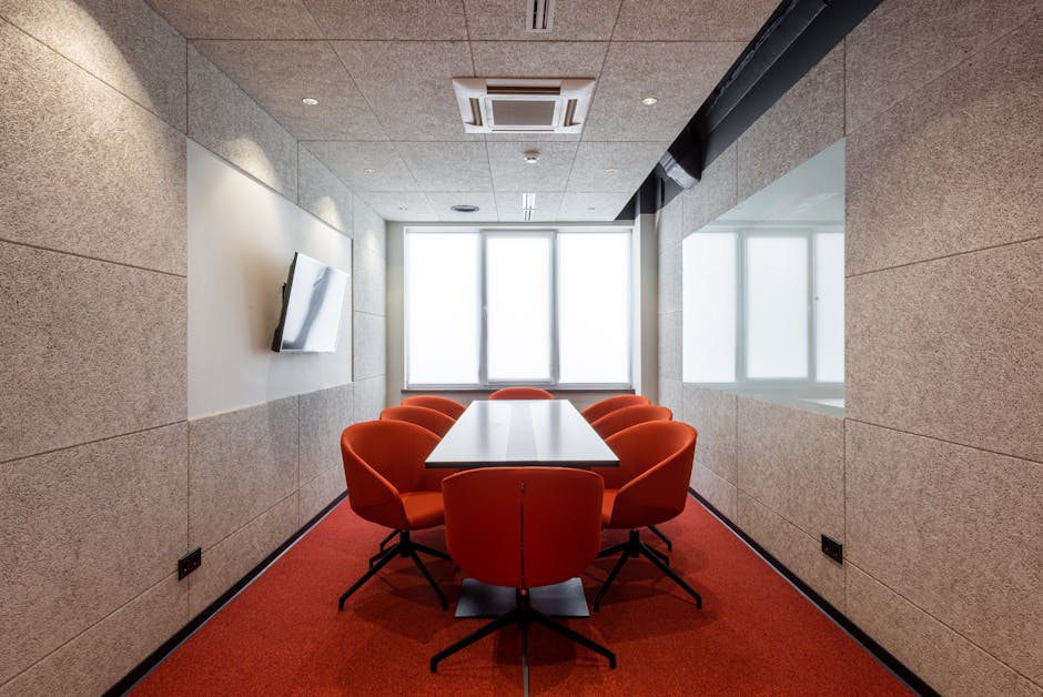 Orange chairs placed around white table in modern conference room with window and TV on wall in contemporary business center