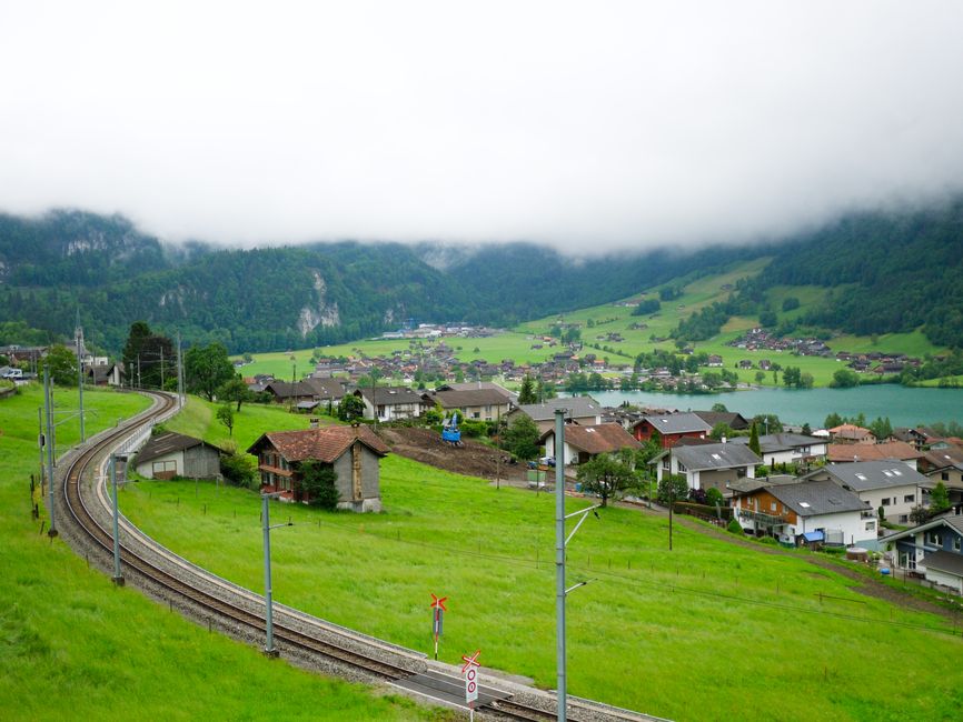 Beautiful shot of Lungern village in Switzerland with lush green hills and railway. Misty mountains in the backdrop.
