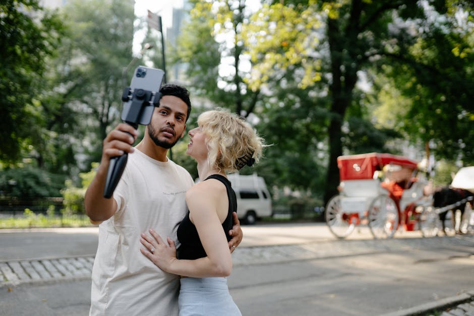 A happy couple takes a selfie outdoors with a carriage in the background.