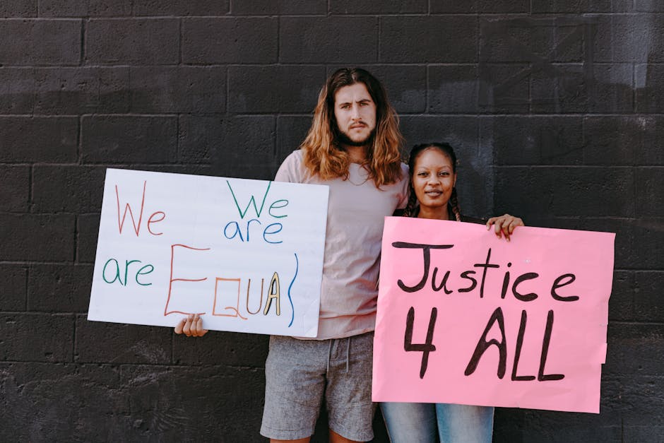 Two people holding equality and justice protest signs against a dark wall.